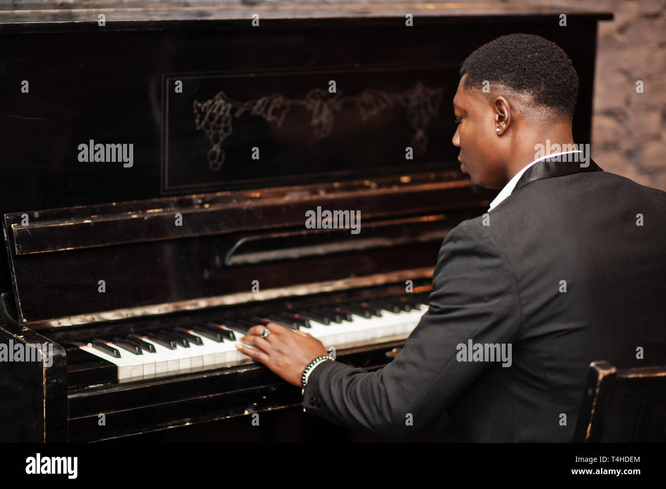 Back of strong powerful african american man in black suit play piano