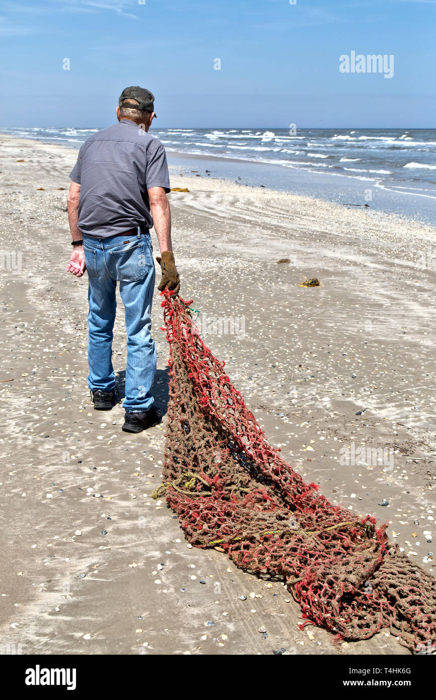Volunteer removing hemp rope cargo net washed ashore with the incoming tide. Stock Photo