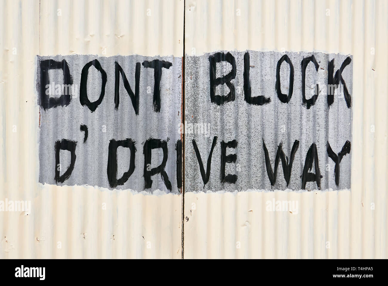 Closed gate of corrugated metal with written sign 'Don't block the driveway'. The gate is newly painted in white color, but the writing is spared. Stock Photo