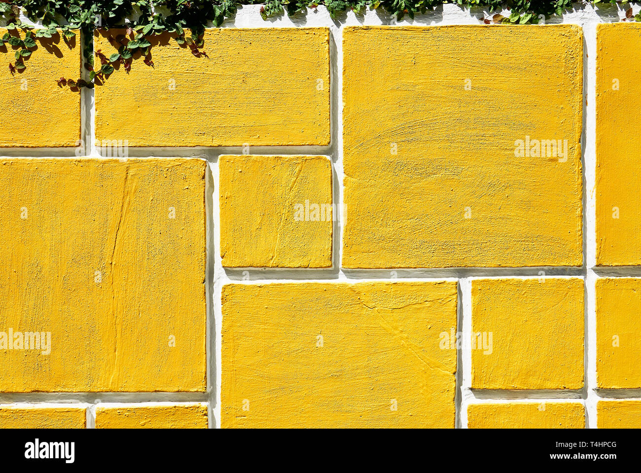 Detail of a rectangle shaped grid design of a concrete garden wall fence painted in bright yellow. Green plants hanging from the top of the wall. Stock Photo