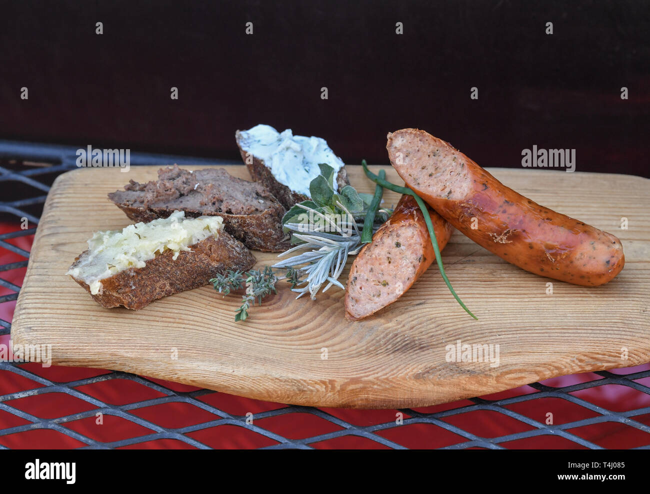 16 April 2019, Brandenburg, Fürstenwalde: Herb smoked sausage from the  charcoal grill coated with stone oven bread with vegetarian lard (l-r),  wild boar liver sausage and wild herb curd cheese are served