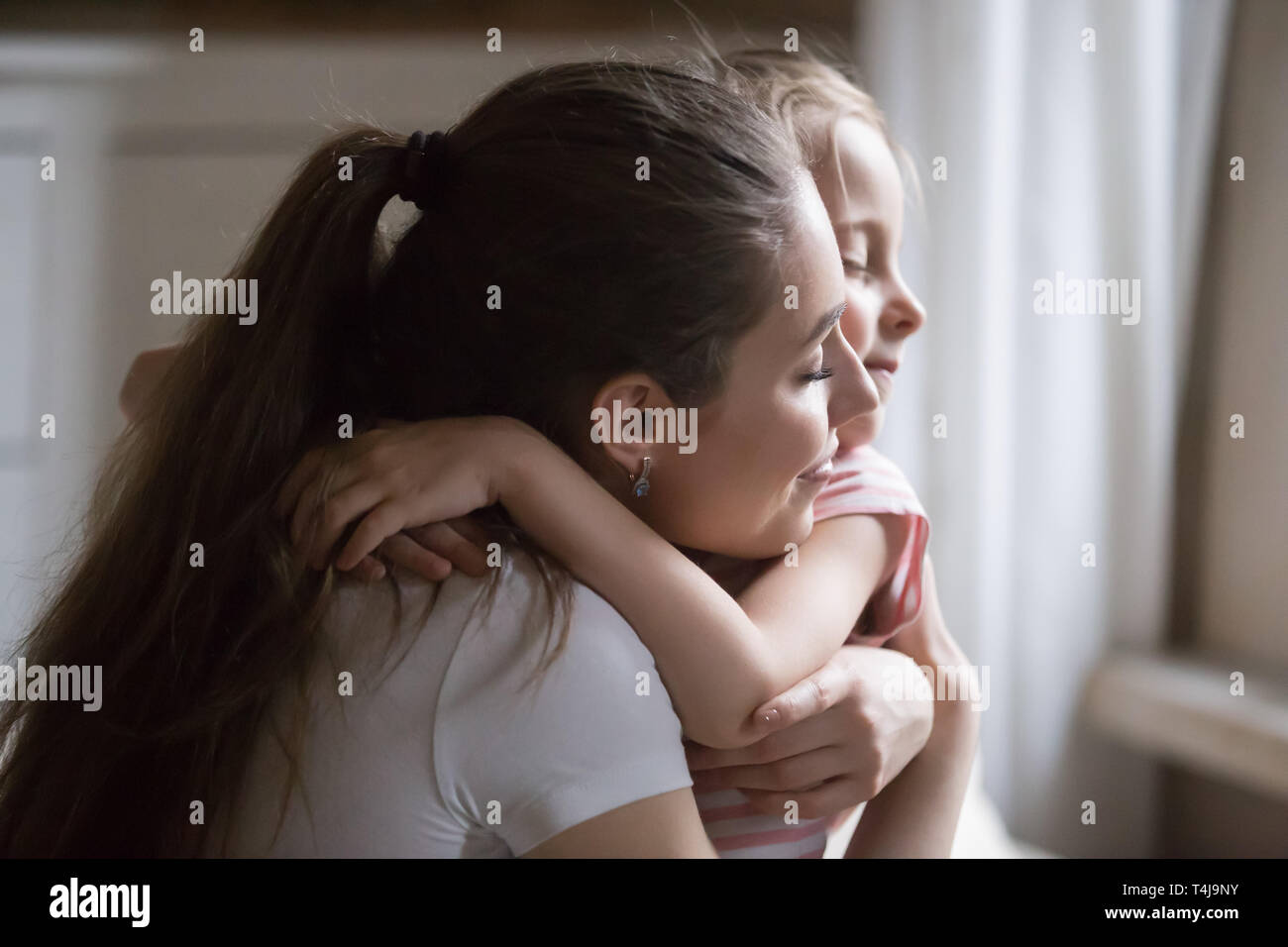 Loving mother give strong hug to daughter with eyes closed Stock Photo