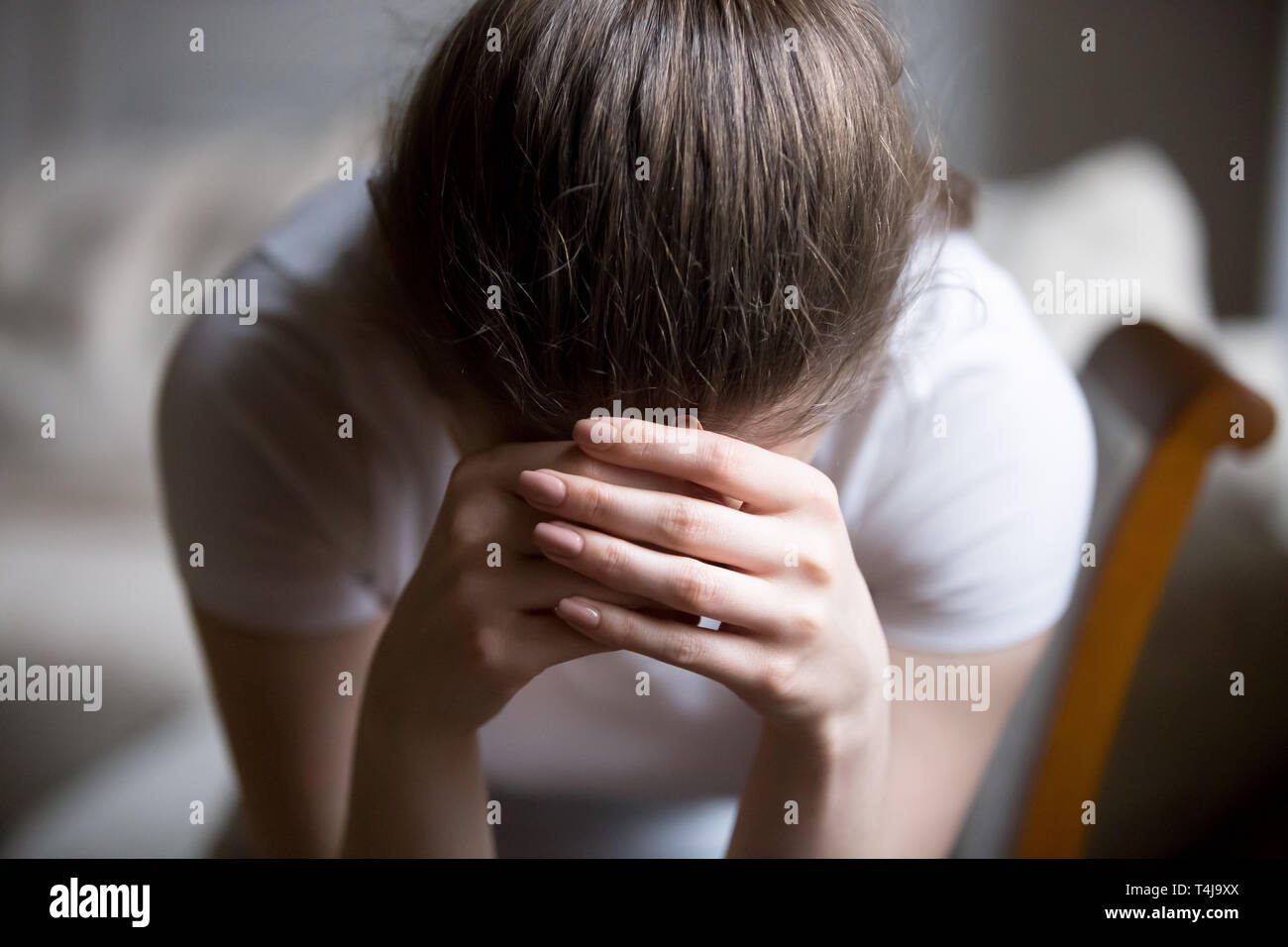 Close up desperate woman sitting on chair crying at home Stock Photo