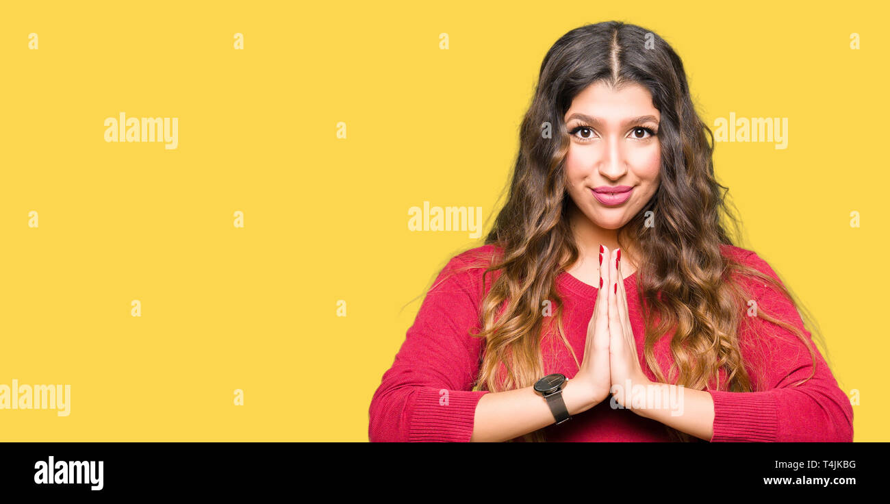 Young beautiful woman wearing red sweater praying with hands together ...