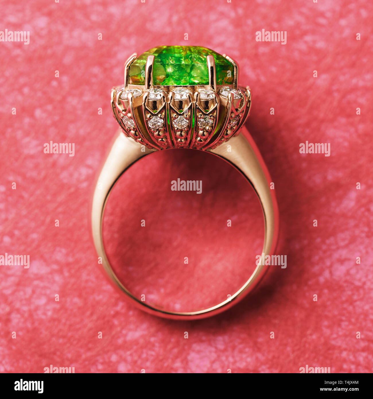 Golden ring with large emerald and small cubic zirconias on a red abstract background Stock Photo