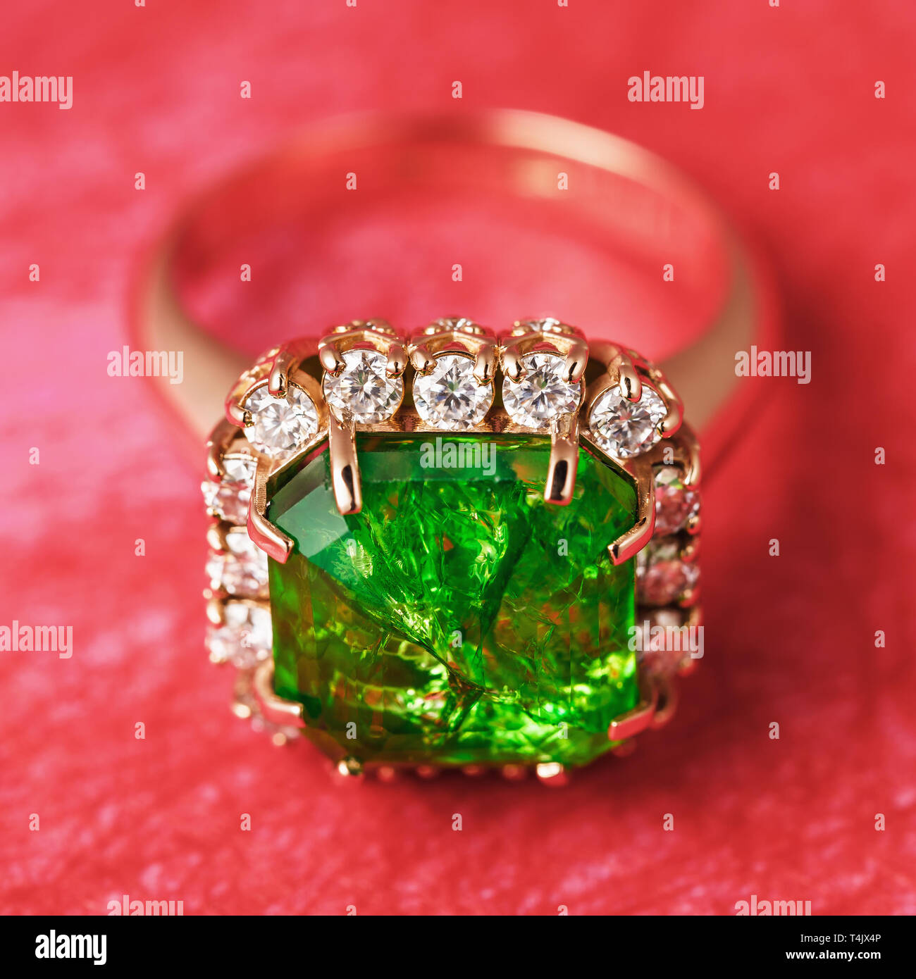 The Golden Ring with a big emerald and a path from small cubic zirconias on a red abstract background, a close up Stock Photo
