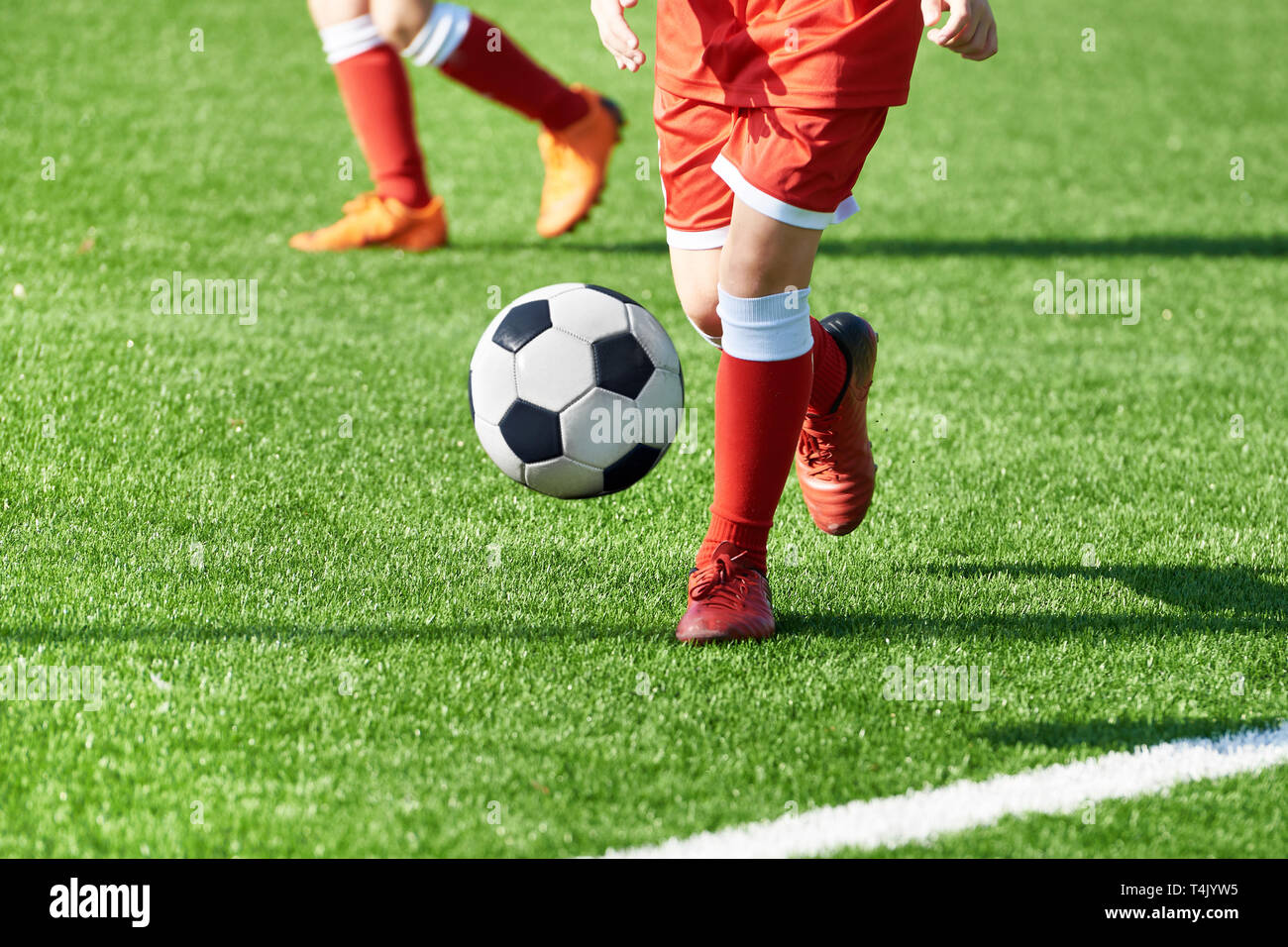 Legs of a soccer player boy in red sports uniform with a ball on a