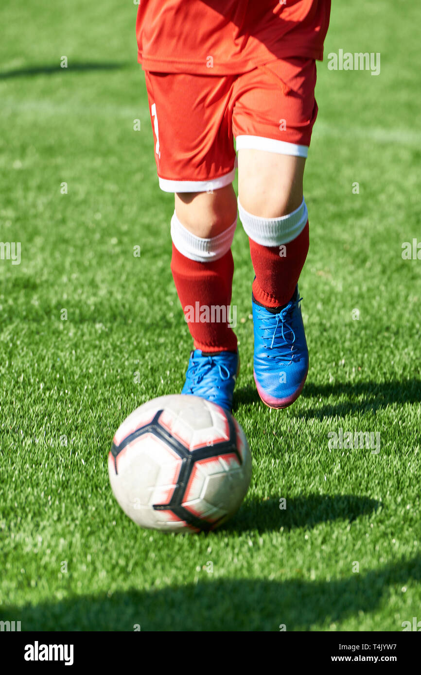 Boy soccer player in red sports uniform with a ball on the football