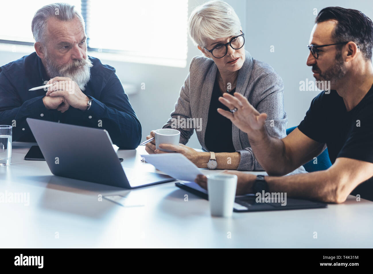 Corporate business team sitting at a table with laptop discussing new project.  Mature man discussing new business ideas with colleagues at office. Stock Photo