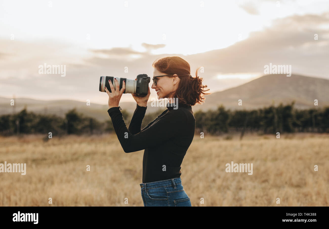 Side view of young female photographer shooting with dslr camera outdoors. Woman having a outdoors photo shoot. Stock Photo