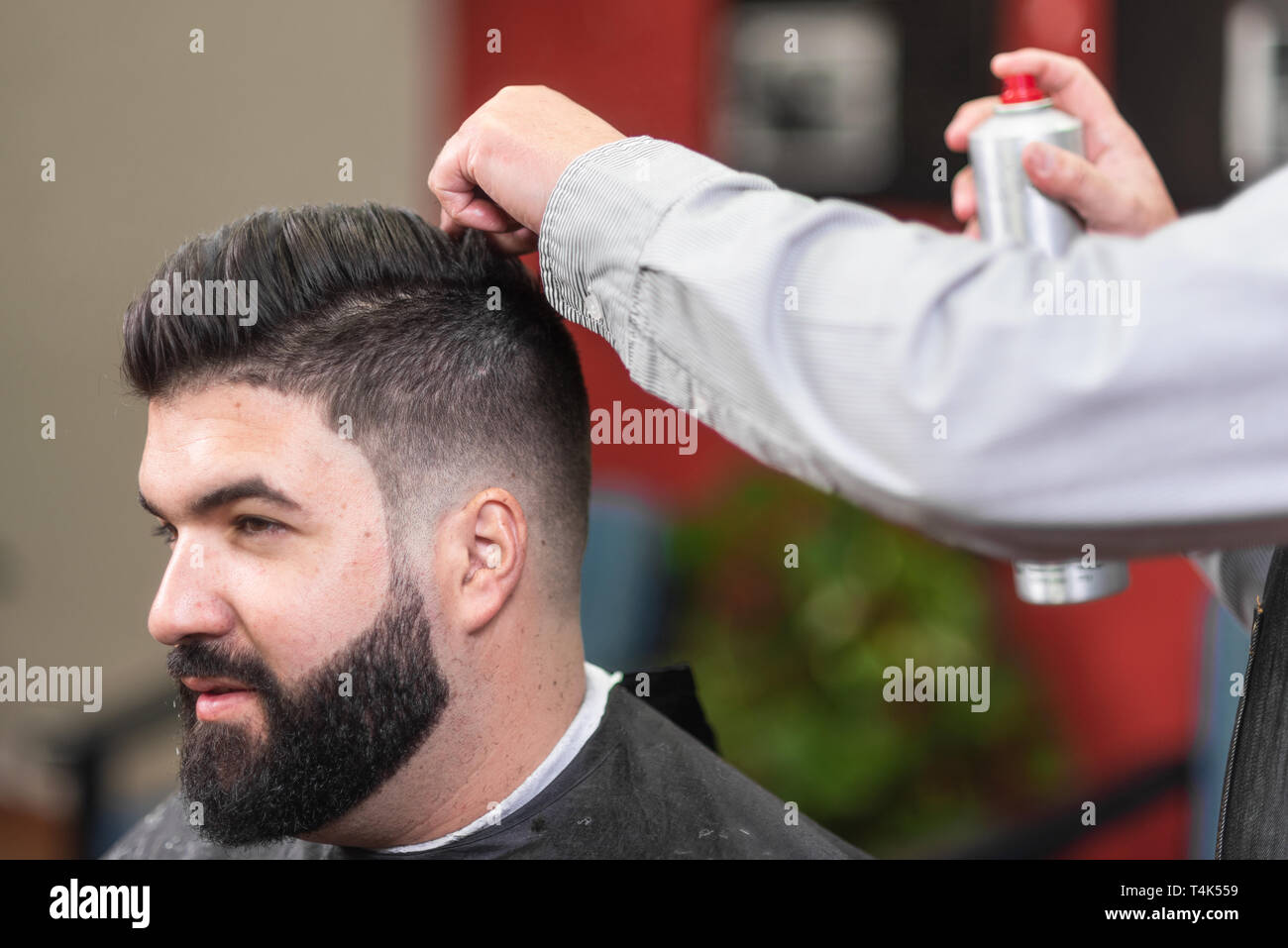 Master barber making modern hairstyle fixating hair with spray . Stock Photo