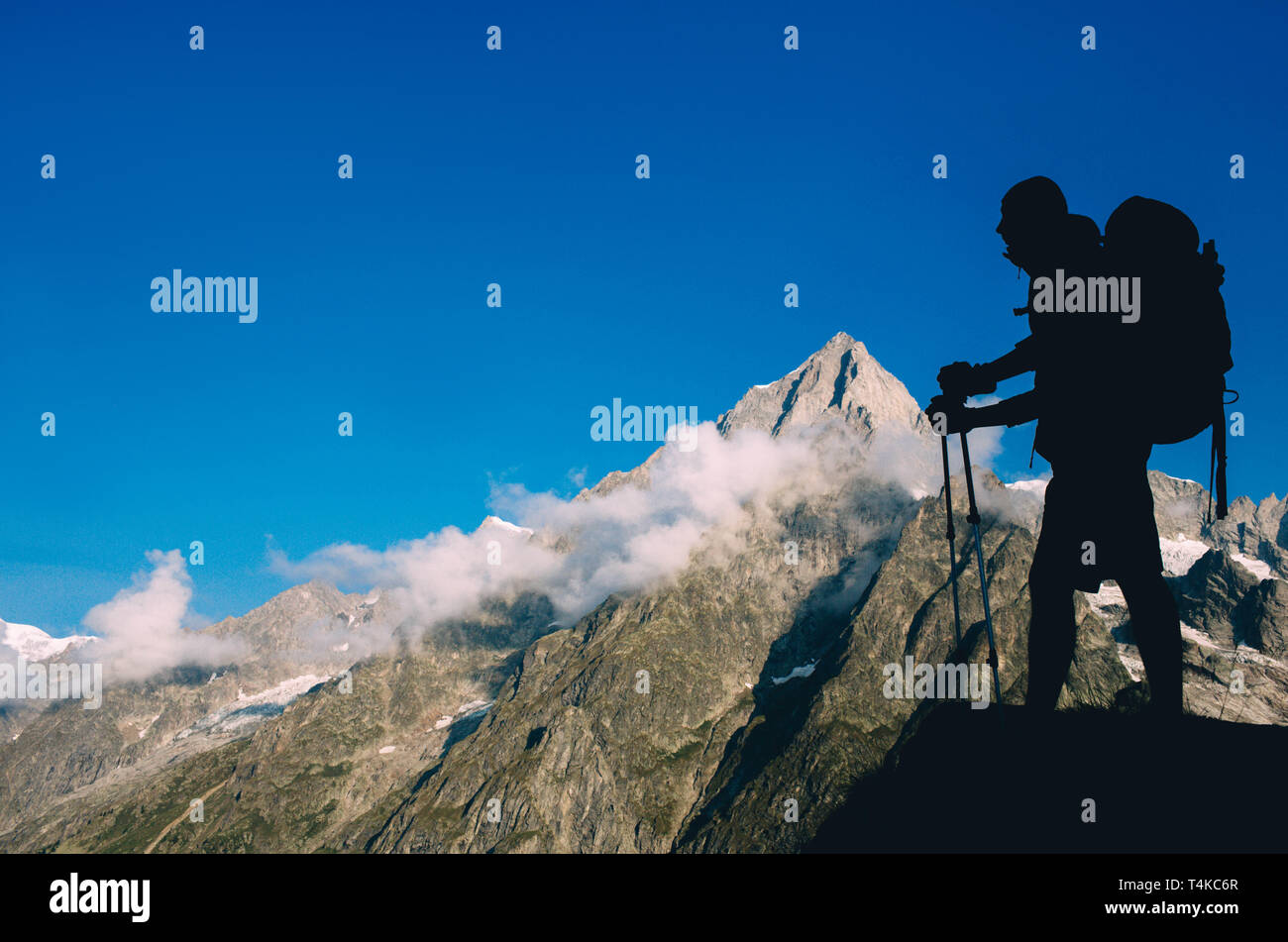 Silhouette man with backpack and trekking pole, hiking over European Alps on the background. Stock Photo