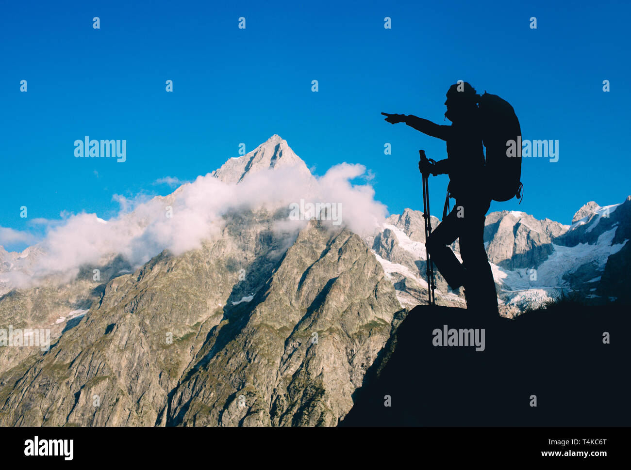 Silhouette woman with backpack and trekking pole, hiking over European Alps on the background. Stock Photo