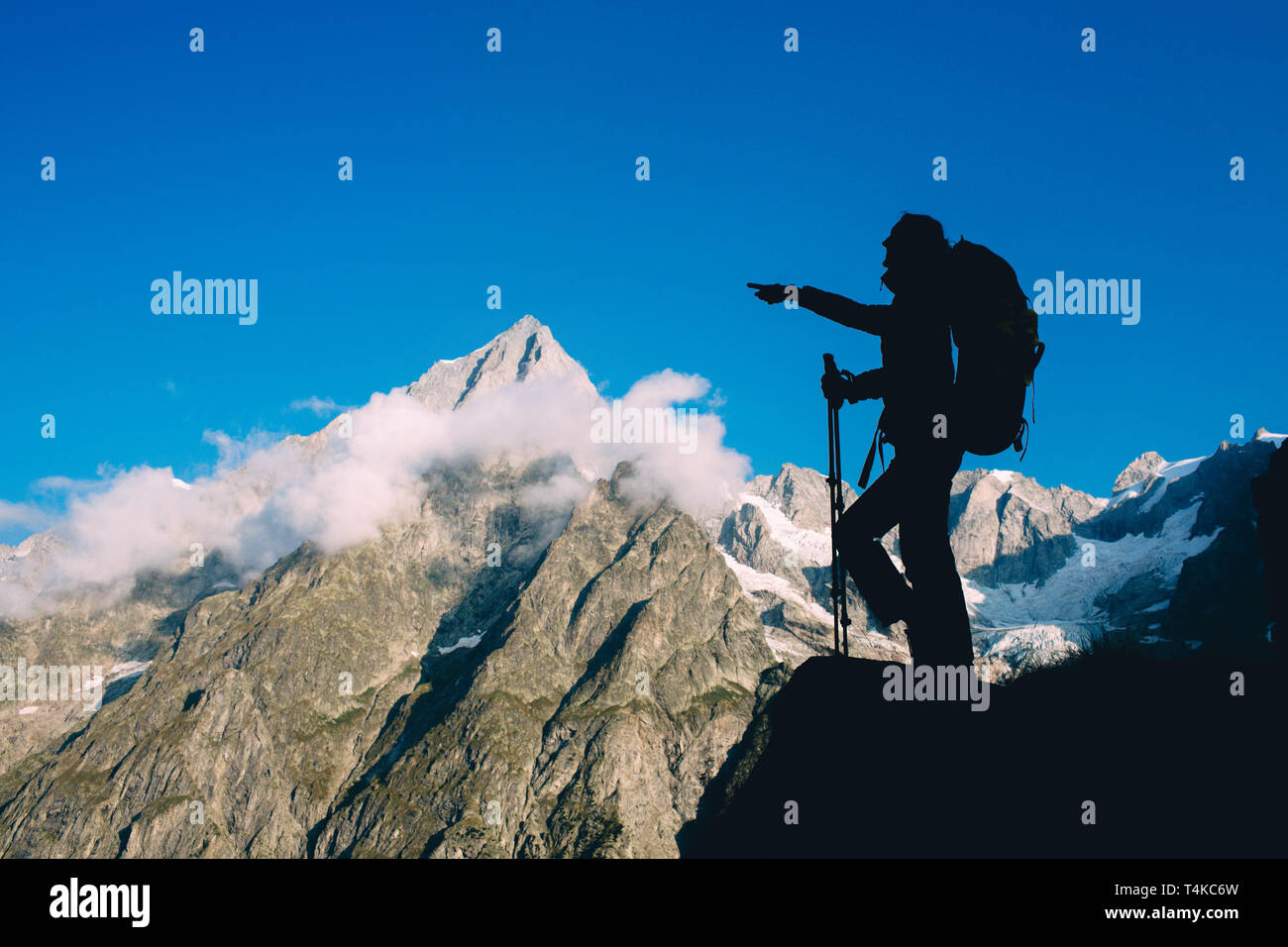 Silhouette woman with backpack and trekking pole, hiking over European Alps on the background. Stock Photo