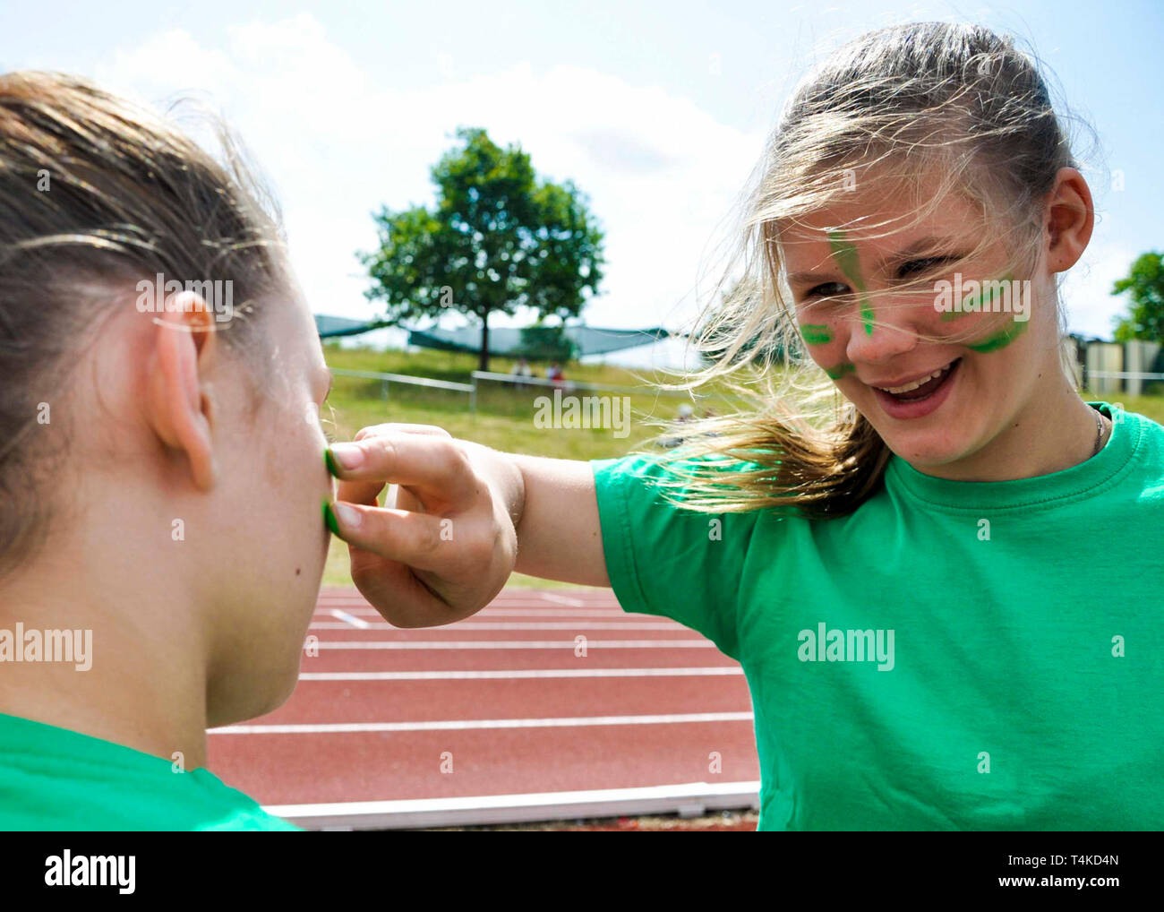 Girl putting green face paint on friend for house athletics day, UK. Stock Photo