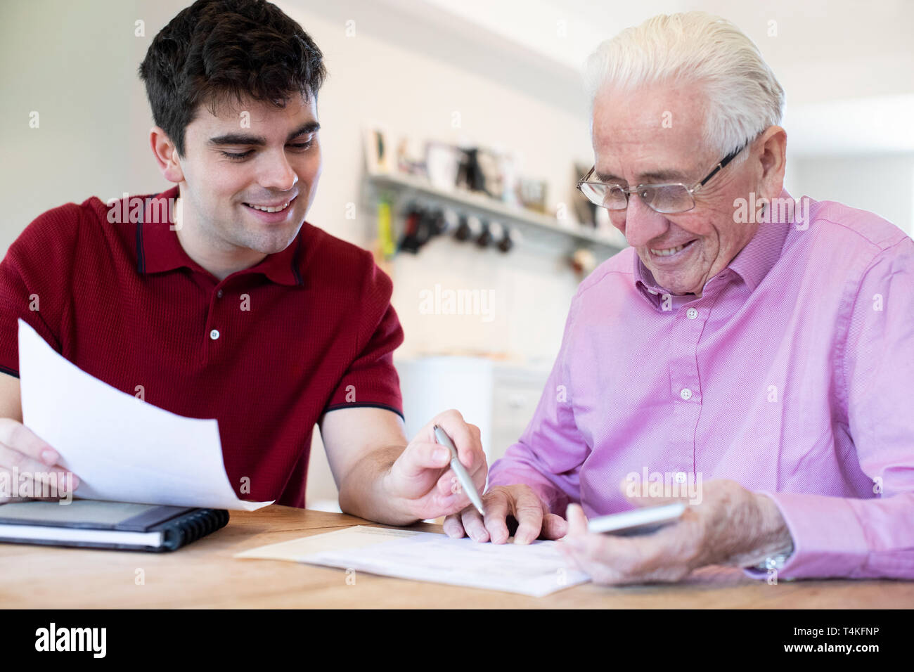 Young Man Helping Senior Neighbor With Paperwork At Home Stock Photo