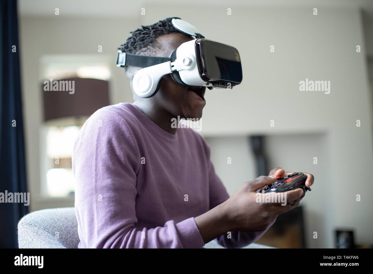Excited Teenage Boy Playing Video Game At Home Wearing Virtual Reality Headset Stock Photo