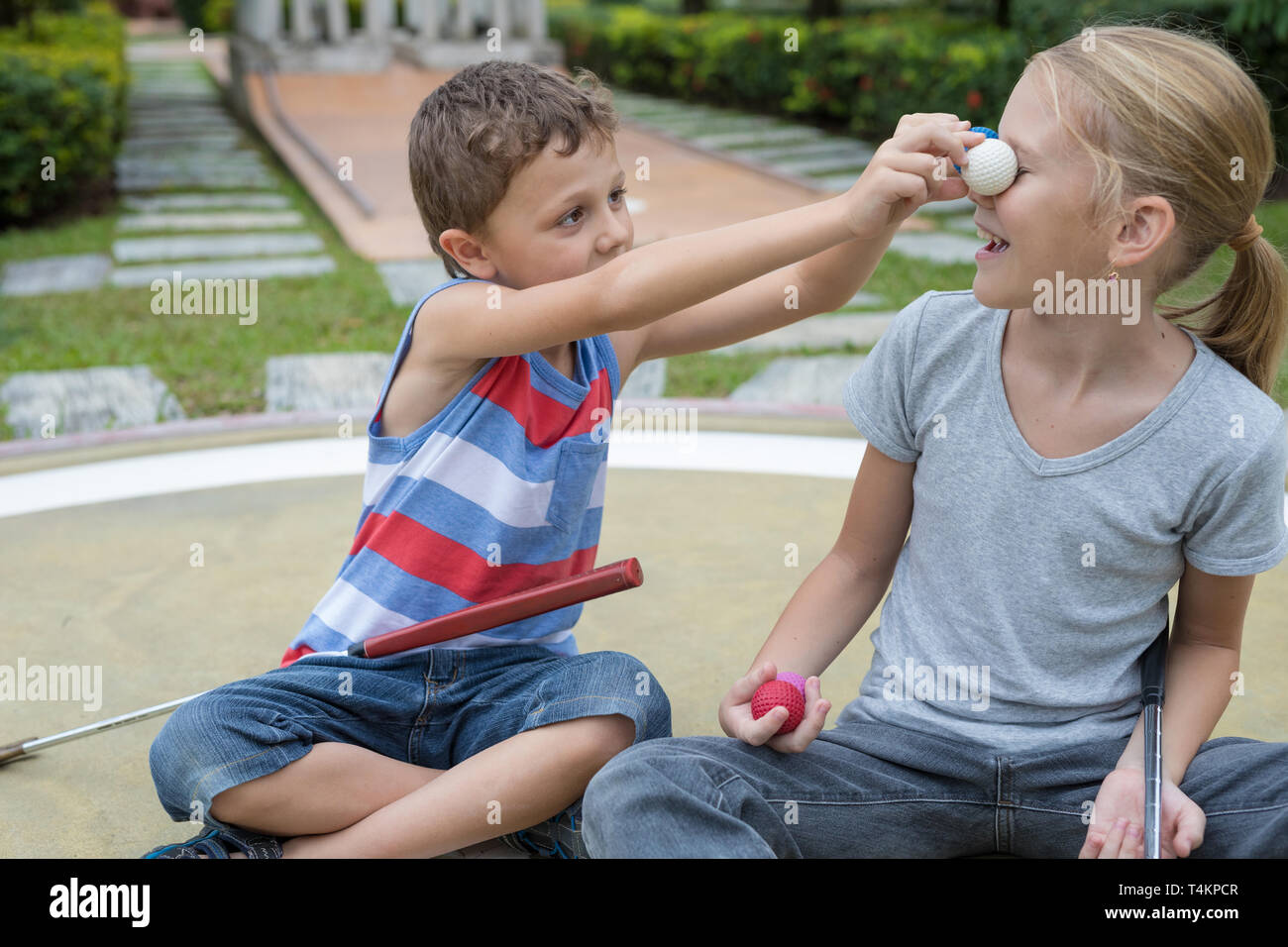 Happy brother and sister playing mini golf  in a park at the day time. People having fun outdoors. Concept of good leisure. Stock Photo