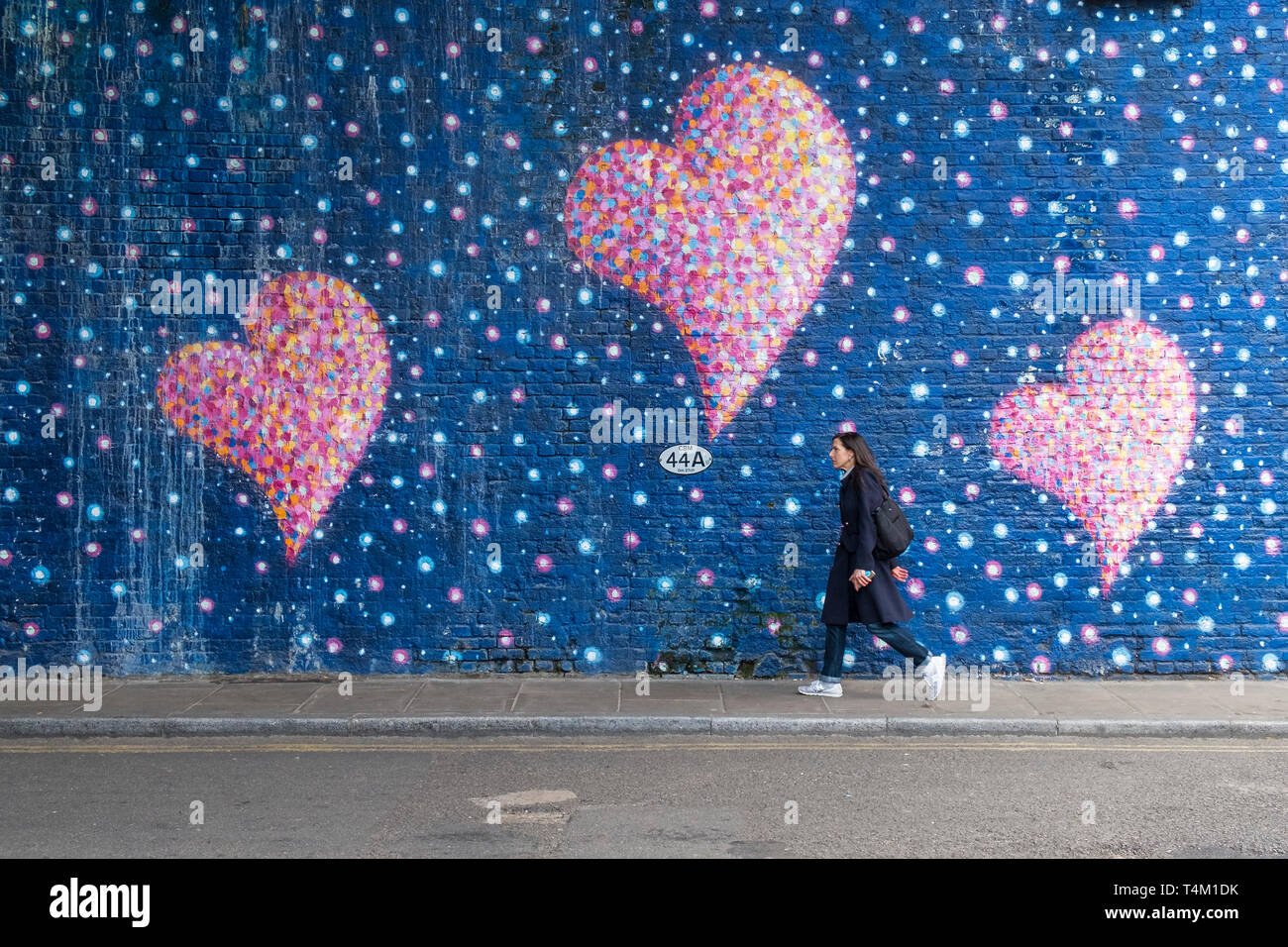 A woman walking past a large painted mural of pink hearts painted by Jimmy C in memory of London Bridge terror attacks. Stock Photo