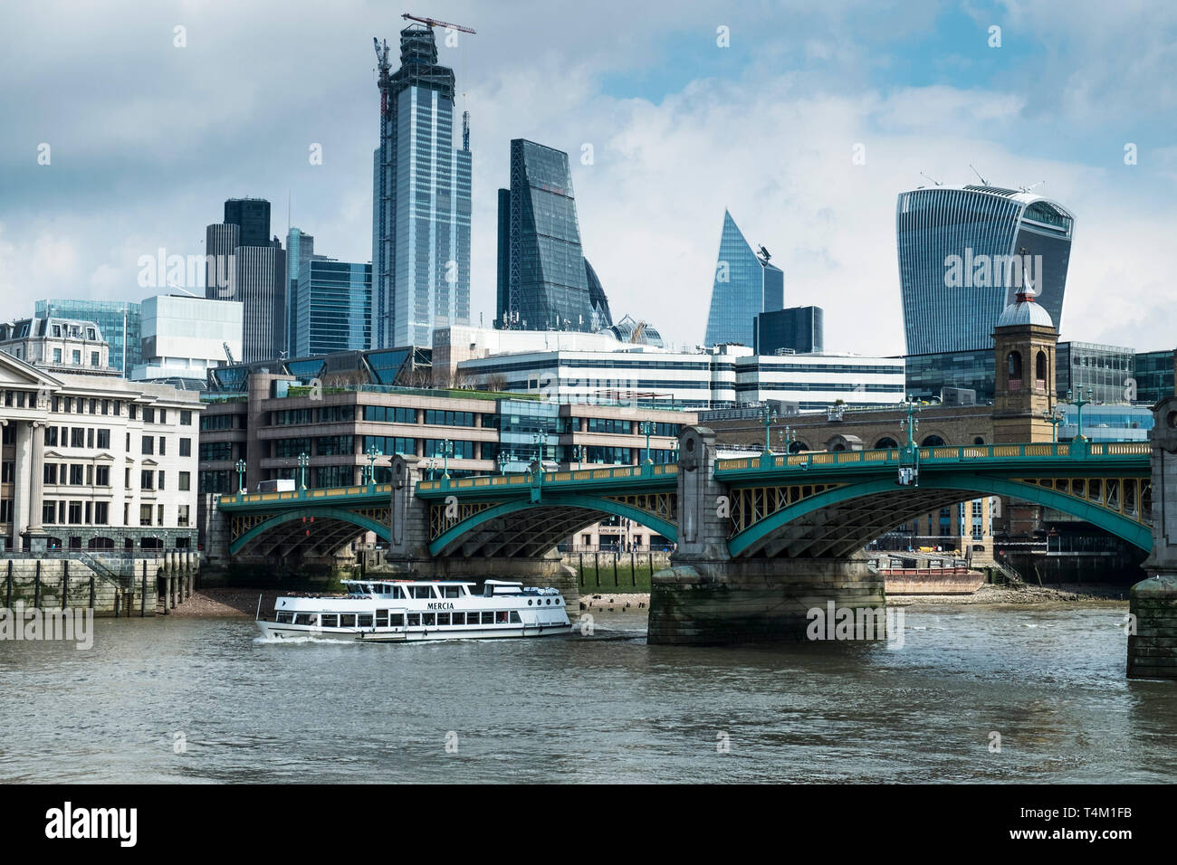 The tourist sightseeing boat Mercia passing under Southwark Bridge on the River Thames with the iconic high rise buildings in the background. Stock Photo