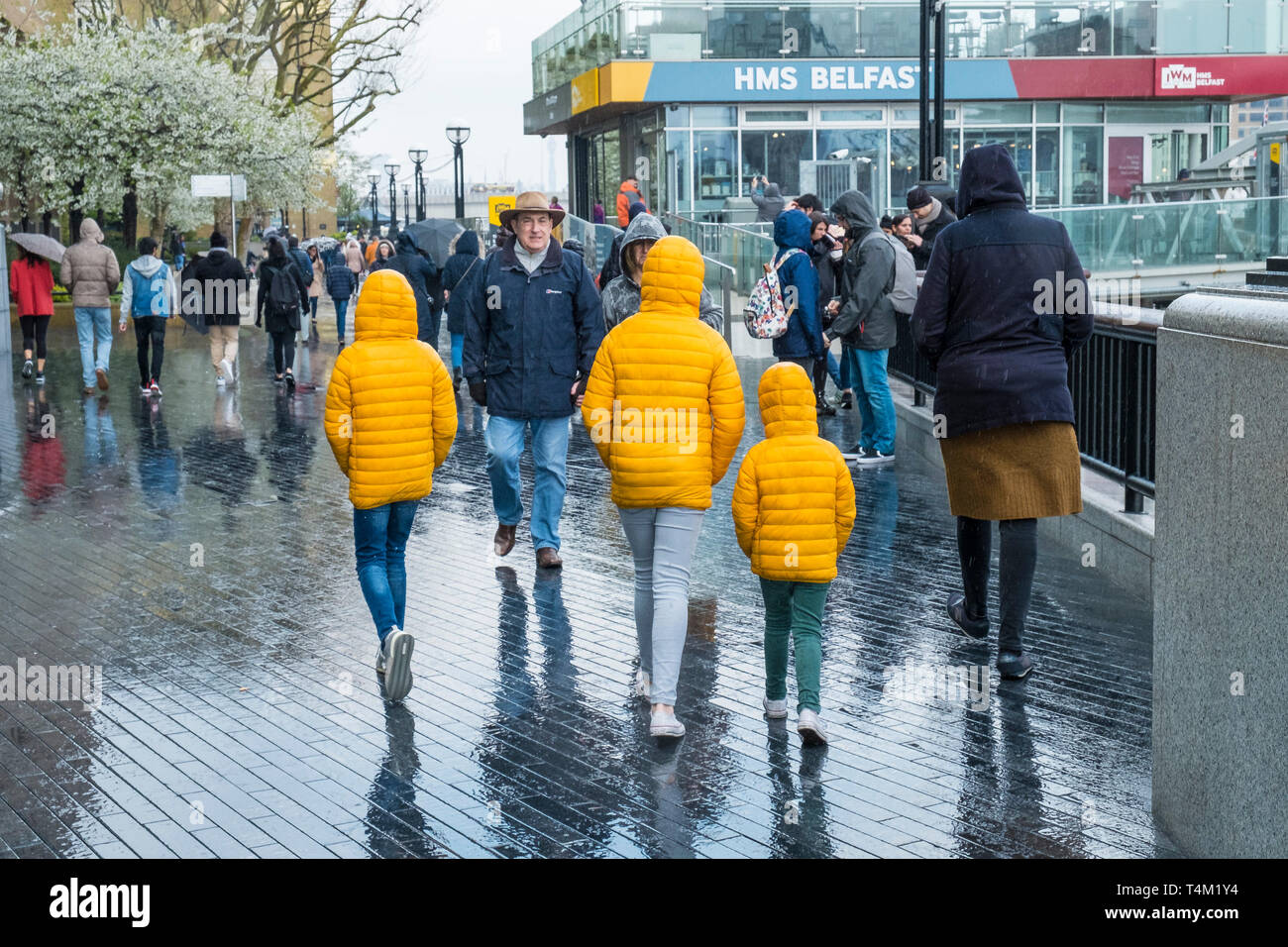 Three children walking along the Southbank in London and wearing matching bright yellow jackets in the rain Stock Photo