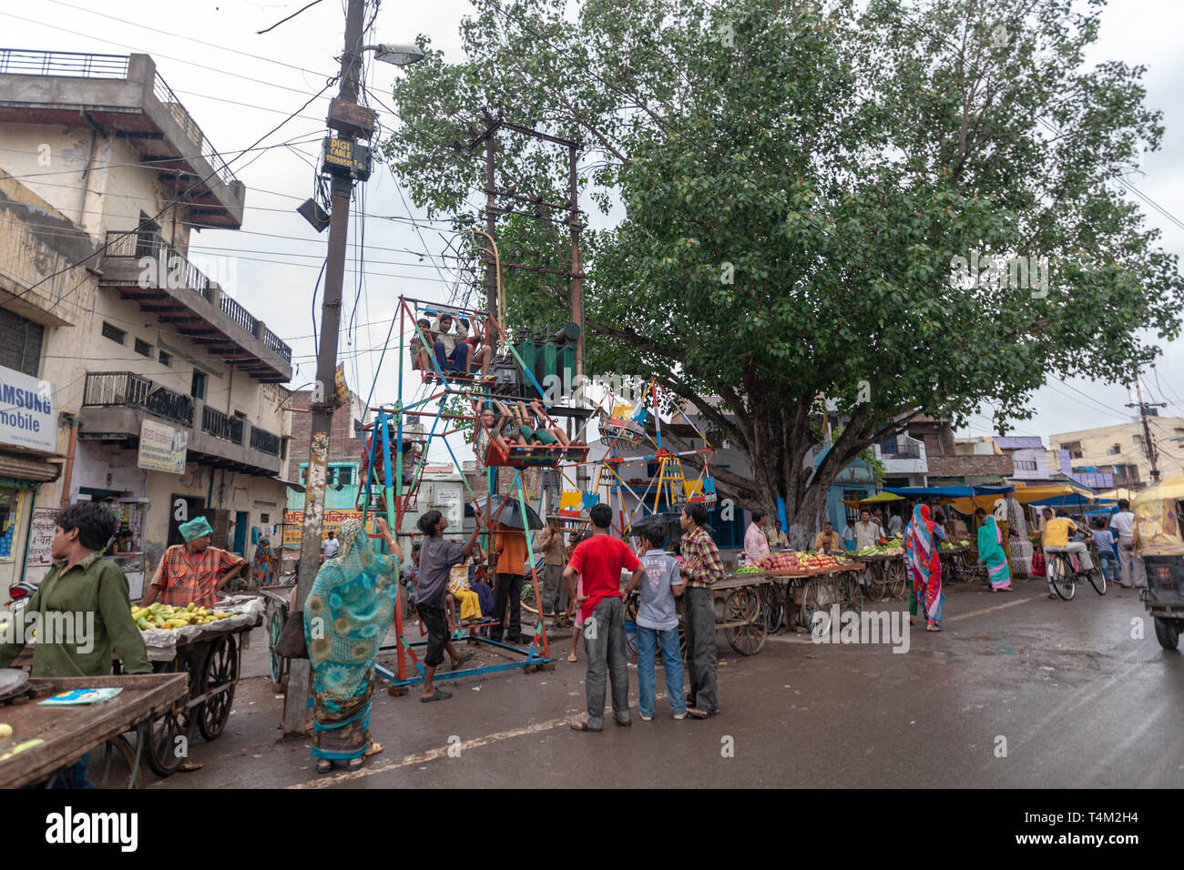 Food stalls in an Agra street with a rudimentary manually operated ferris wheel in Agra, Uttar Pradesh, India Stock Photo
