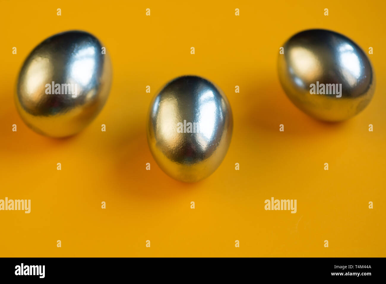three silver eggs lie on a bright yellow background Stock Photo