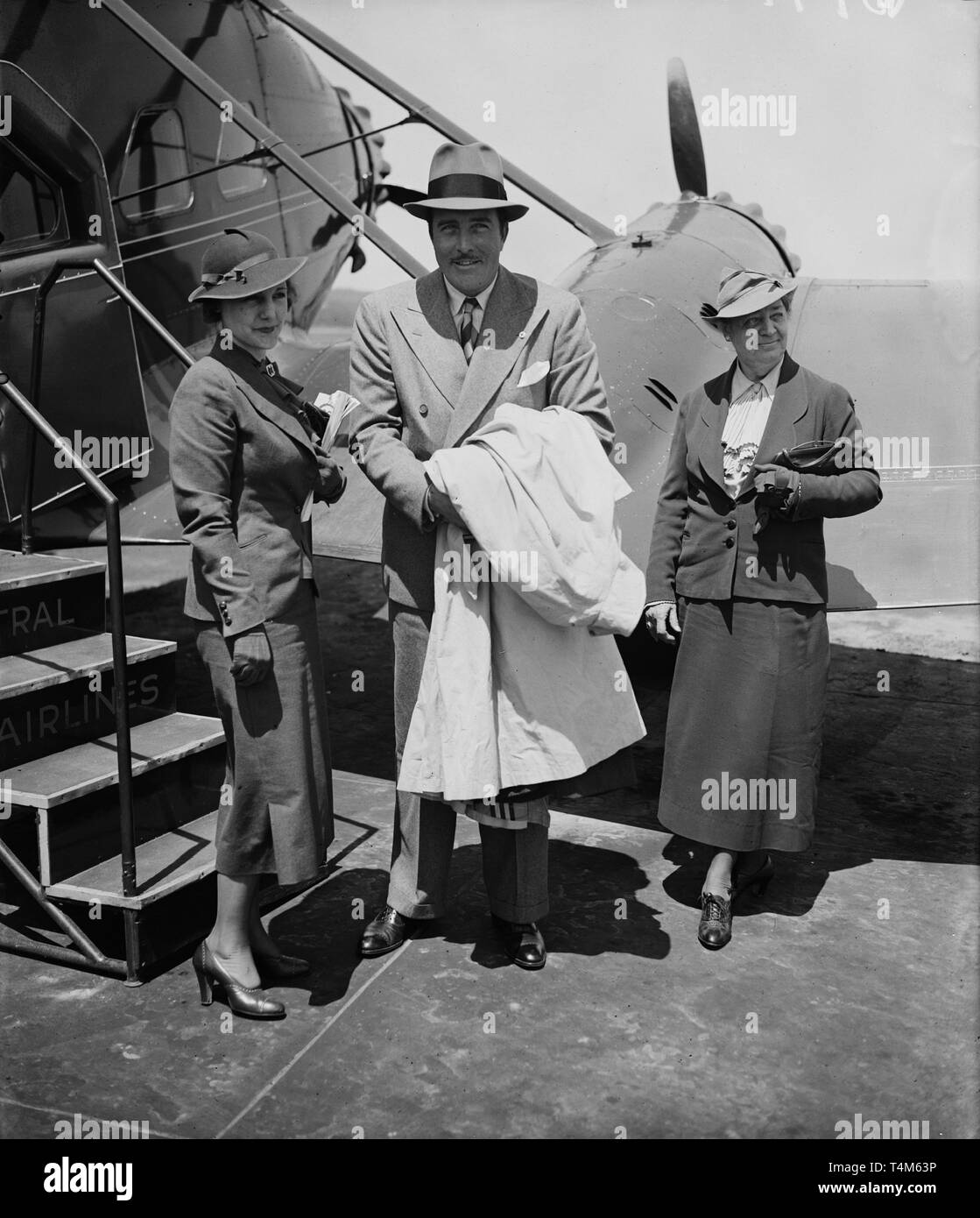 a dapper 40s gent and 2 ladies standing beside an airplane Stock Photo