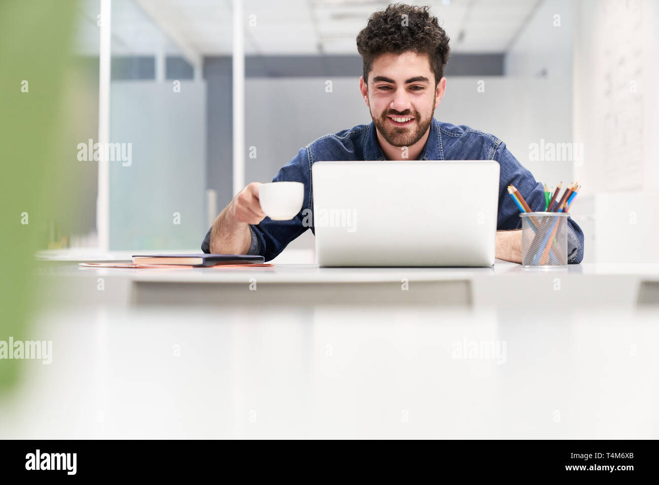 Young programmer is working on laptop. Computer in the office while having coffee Stock Photo