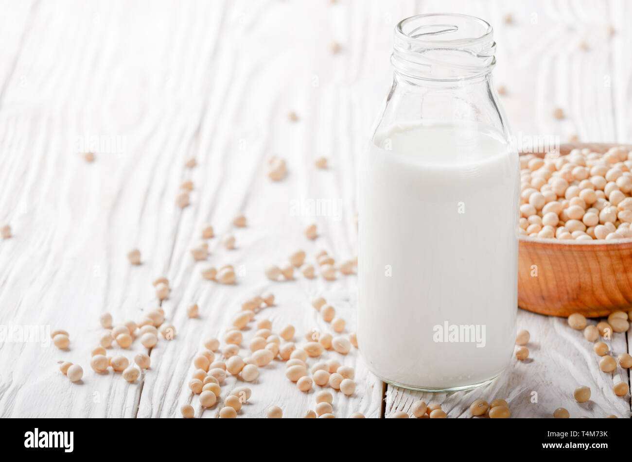 Non-dairy alternative Soy milk or yogurt in glass bottle on white wooden table with soybeans in bowl aside Stock Photo
