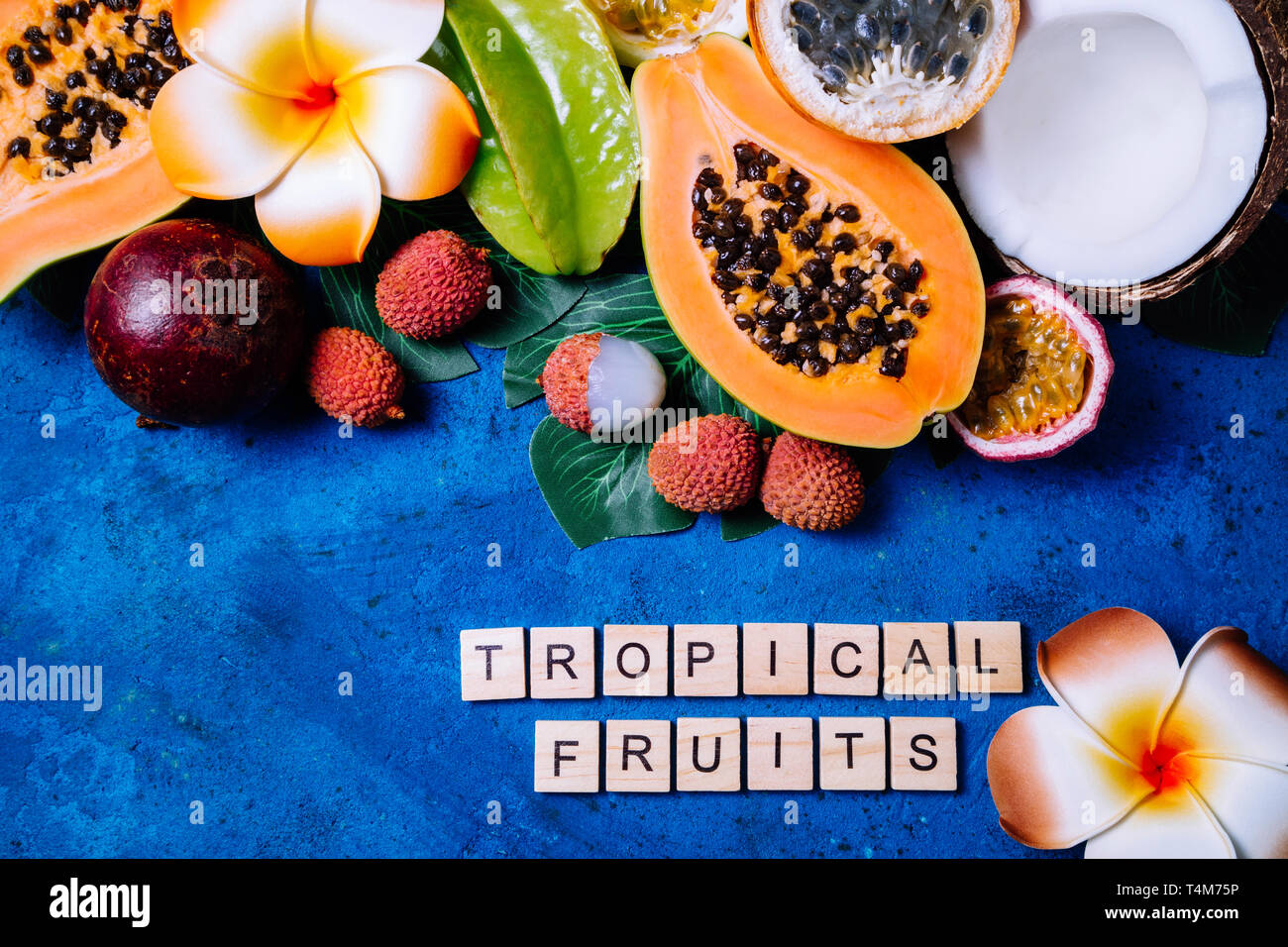 Summer tropical background with exotic various fruits, green palm leaves and flowers on blue. Fruits background. Top view Stock Photo