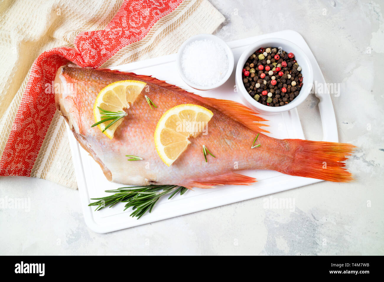 Fish raw snapper with lemon slices, herbs rosemary, salt and pepper on white background. Healthy food and dieting concept. Ingredients for cooking fis Stock Photo