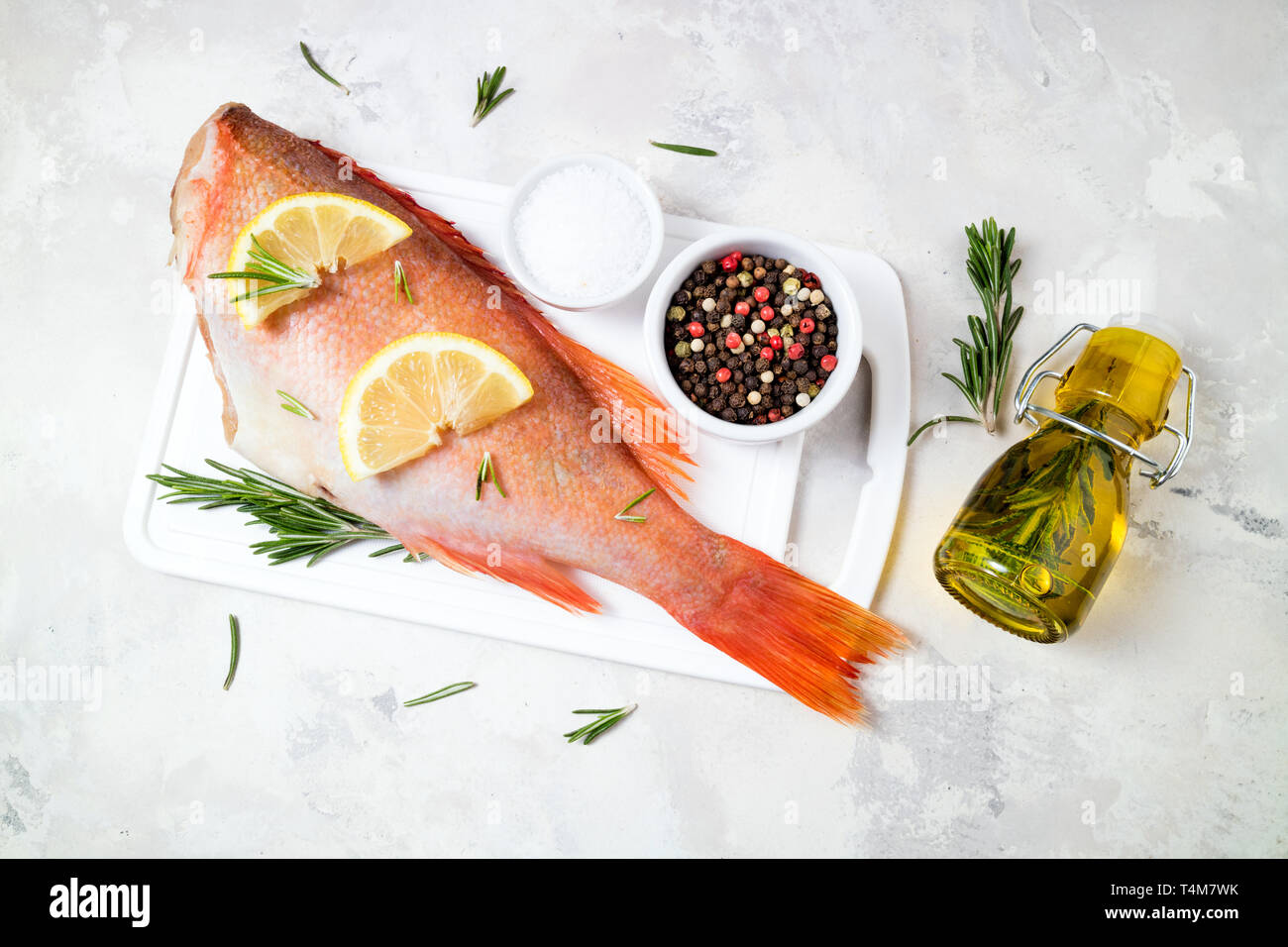 Fish raw snapper with lemon slices, herbs rosemary, salt and pepper on white background. Healthy food and dieting concept. Top view, copy space Stock Photo