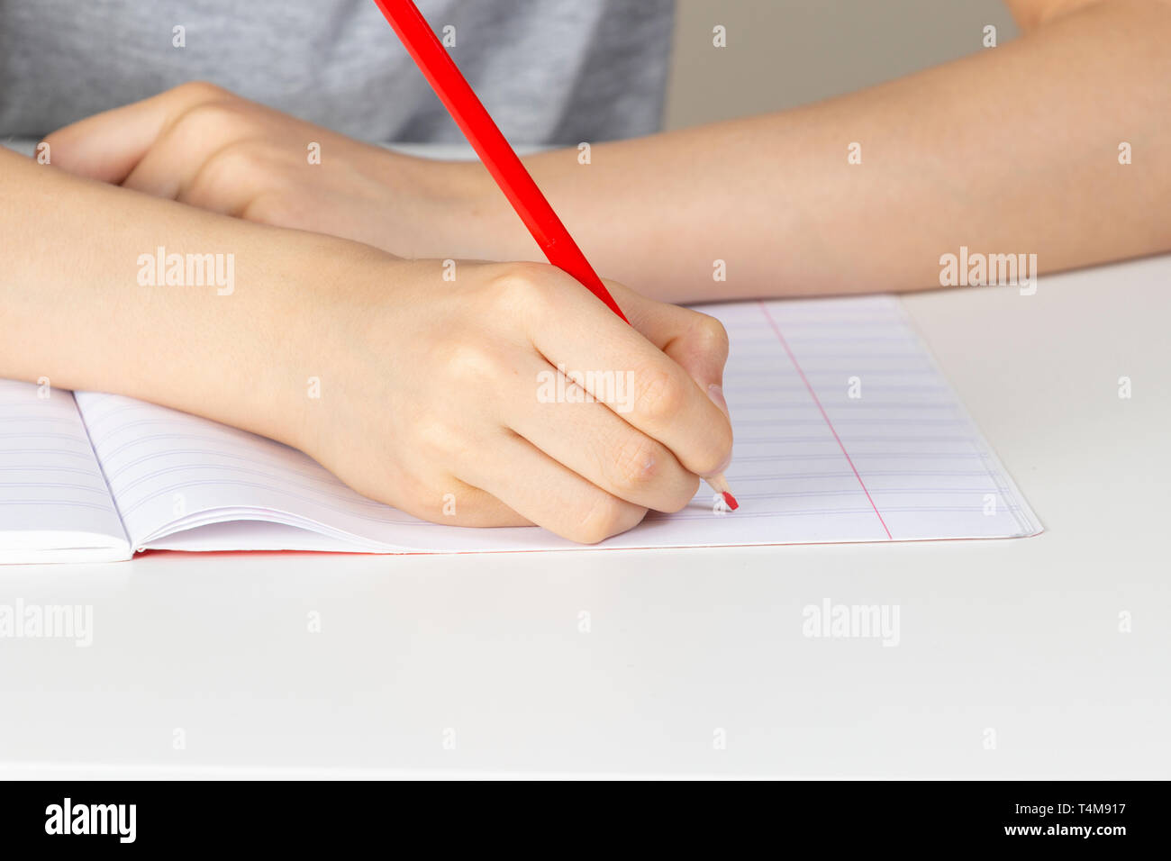 Kid hand holding red pencil against blank page of notebook. Stock Photo