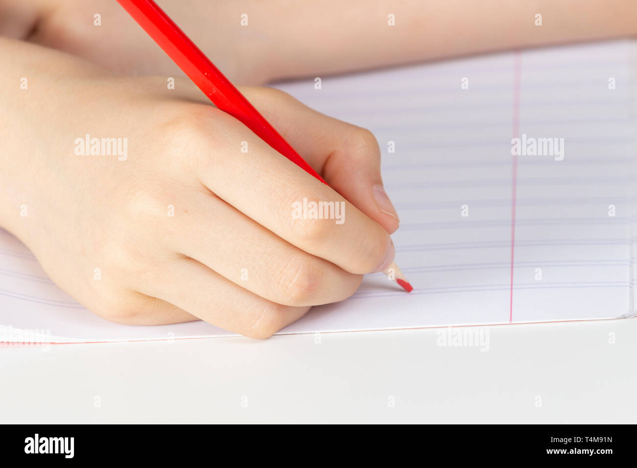 Kid hand holding red pencil against blank page of notebook Stock Photo