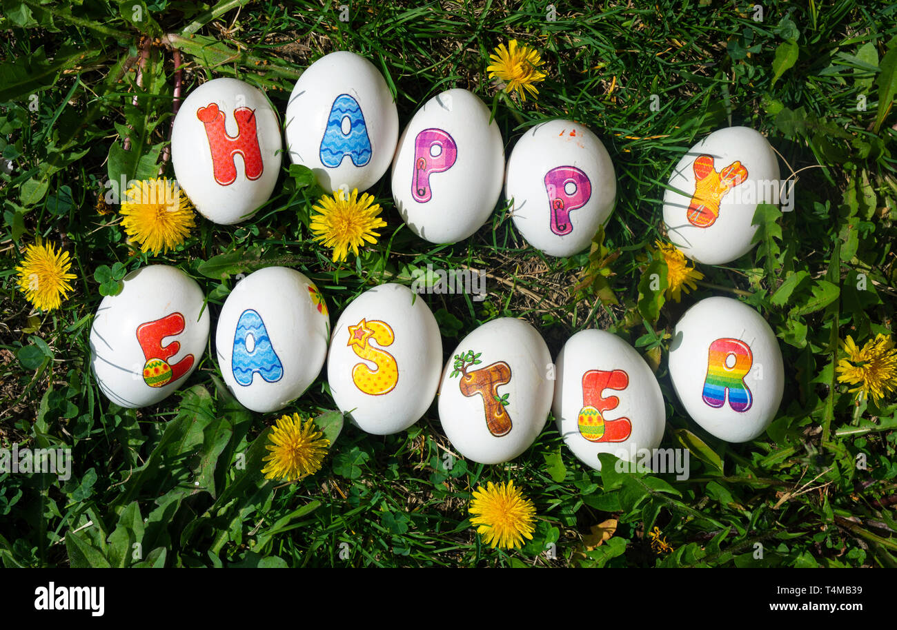 Happy Easter note written on eggs on the grass with yellow dandelions Stock Photo