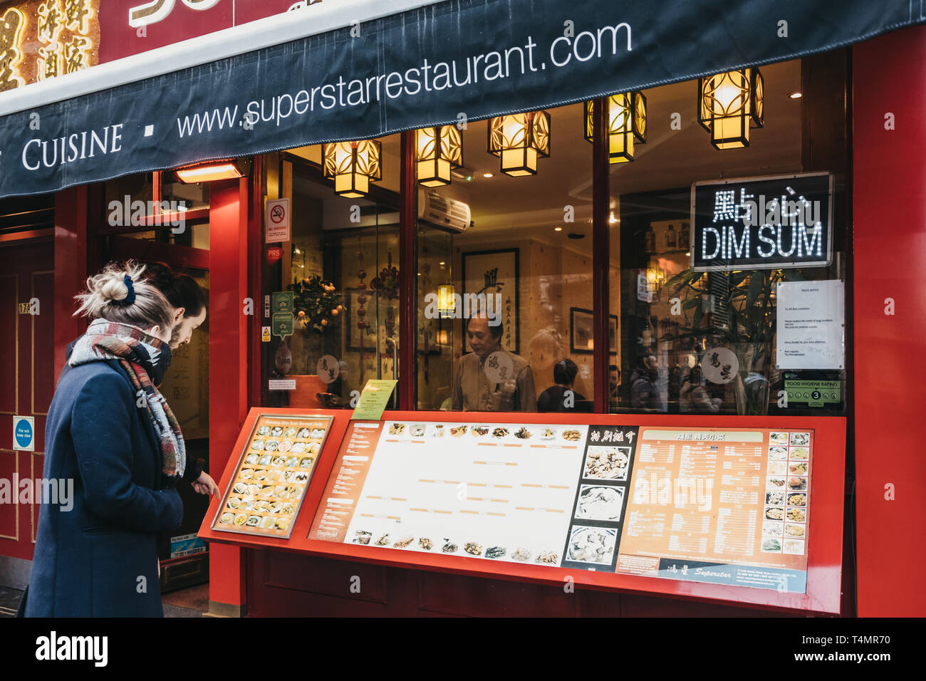 London, UK - April 13, 2019: People standing and reading a menu outside a restaurant in Chinatown, London. Chinatown is home to a large East Asian com Stock Photo