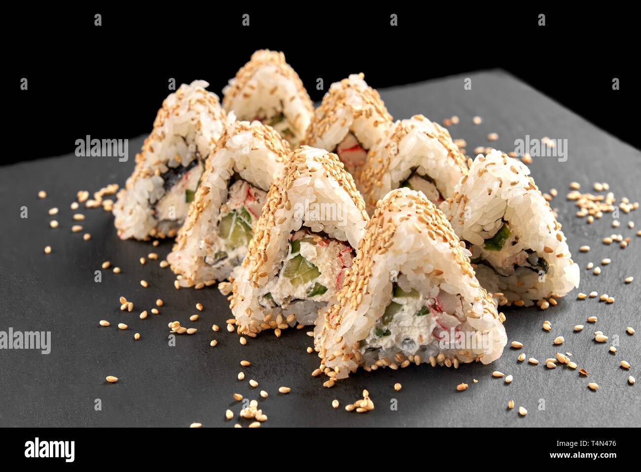 Tasty triangle california uramaki filled with cream cheese, cucumber and  artificial crab meat. Sushi covered with sesame, presented on black stone  slate plate Stock Photo - Alamy