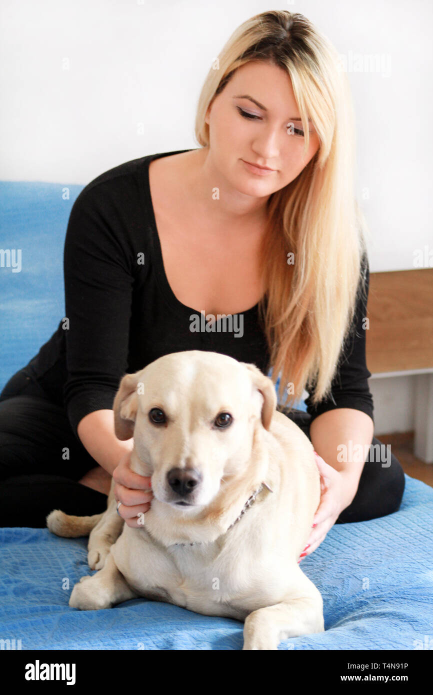 Woman with her dog in bed at home, relaxing in bedroom. Beautiful girl