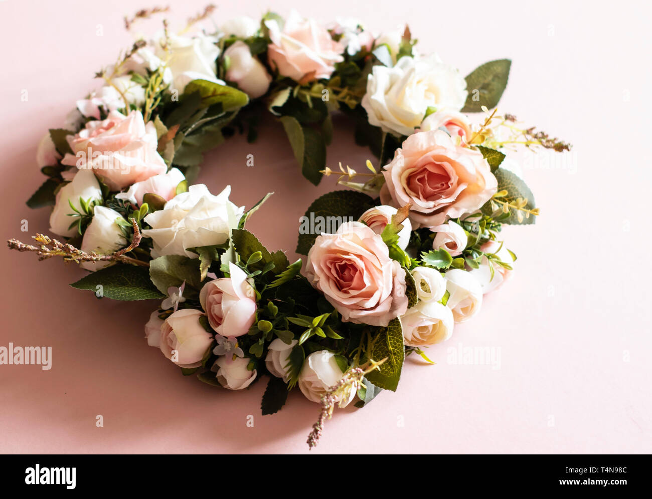 Fake pink rose wreath on a pink background with fake leaves close up