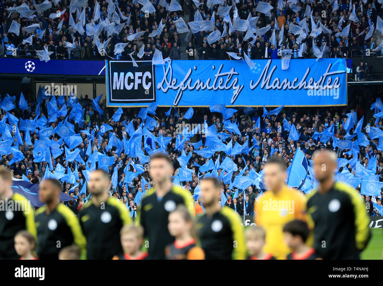Manchester City fans wave flags ahead of kick-off near a banner that reads 'MCFC Definitely Manchester' during the UEFA Champions League quarter final second leg match at the Etihad Stadium, Manchester. Stock Photo