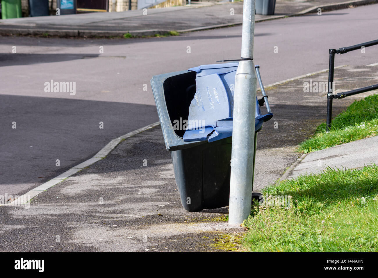 An empty blue recycling wheelie bin with a broken blue lid has been