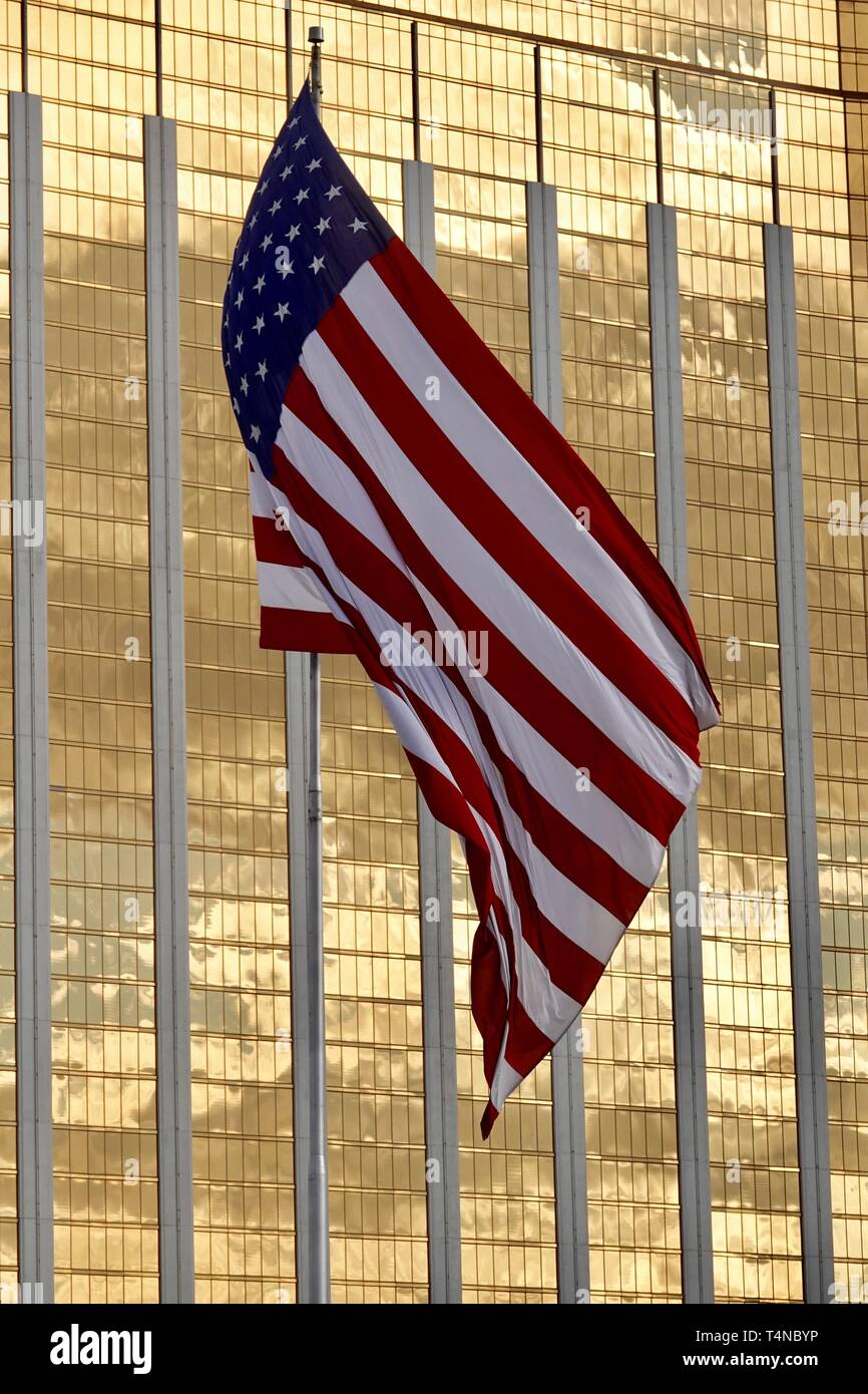 An American flag blows in the wind in front of a yellow glass high rise building. Stock Photo