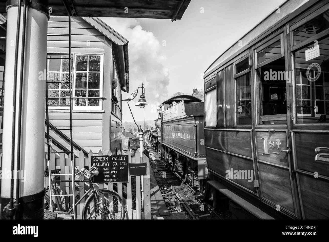 Black & white morning scene on vintage steam railway line, UK. Vintage steam train departure, Bewdley station; signalman in signal box watching train. Stock Photo