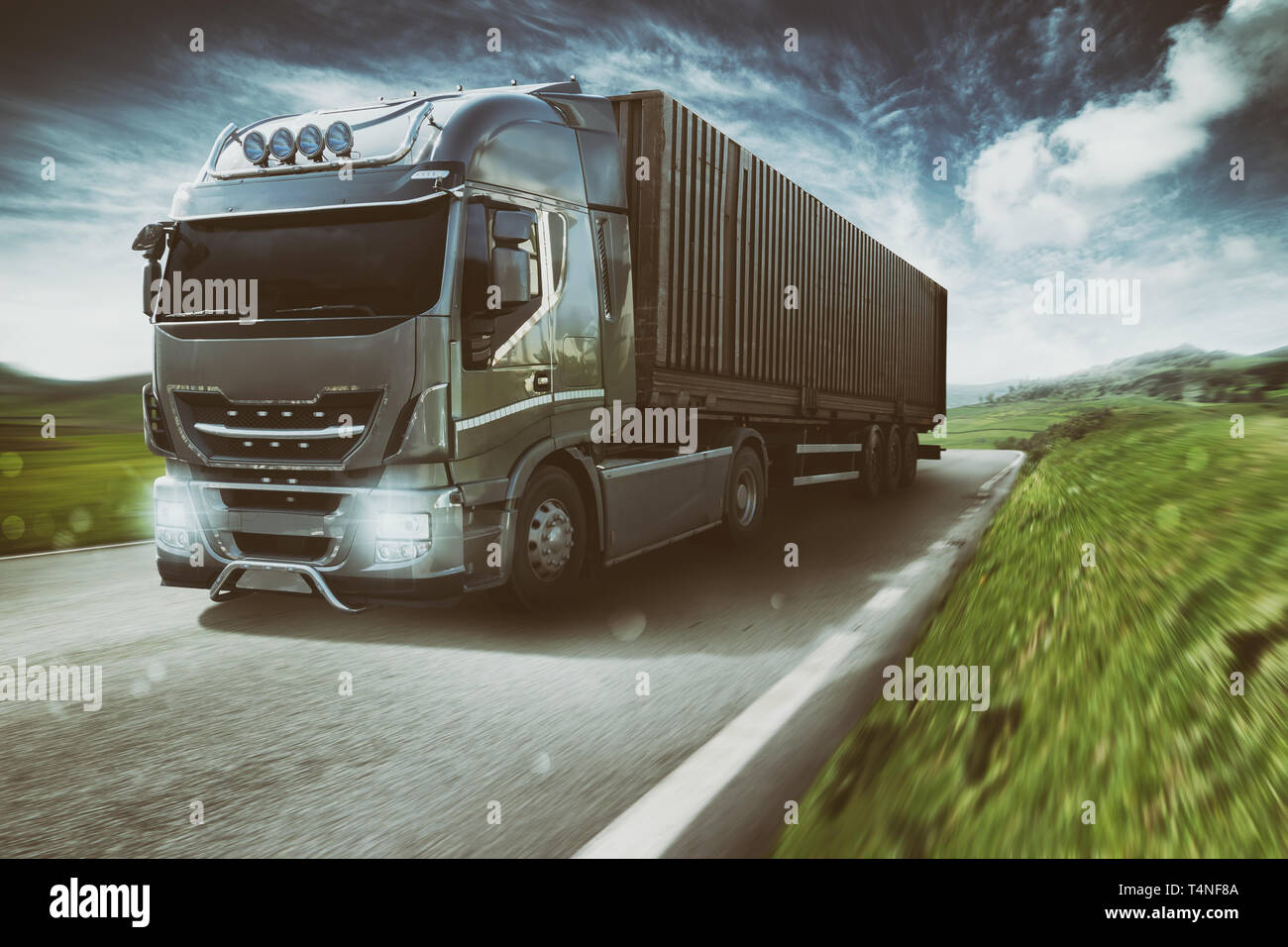 Grey truck moving fast on the road in a natural landscape with cloudy sky Stock Photo