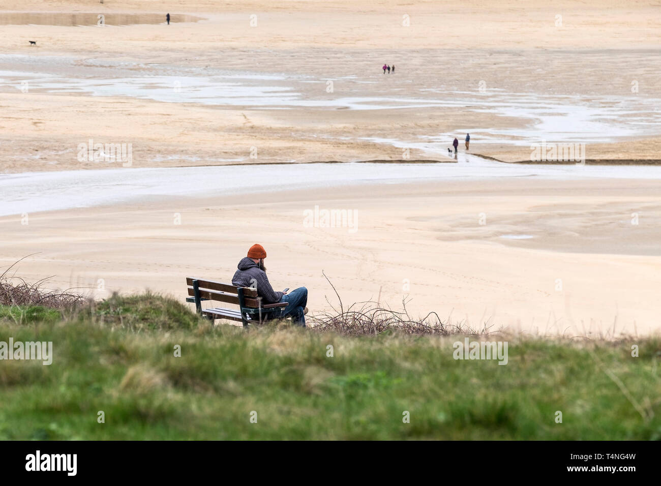 A man sitting alone on a bench overlooking Crantock Beach in Newquay in Cornwall. Stock Photo