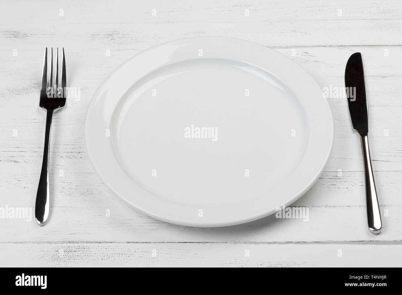Empty clean plate with fork and knife on wooden table, focus on front part Stock Photo