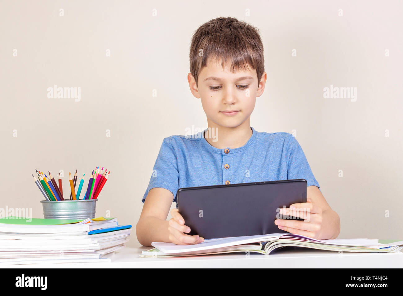 Kid sitting at table with books notebooks and using tablet computer