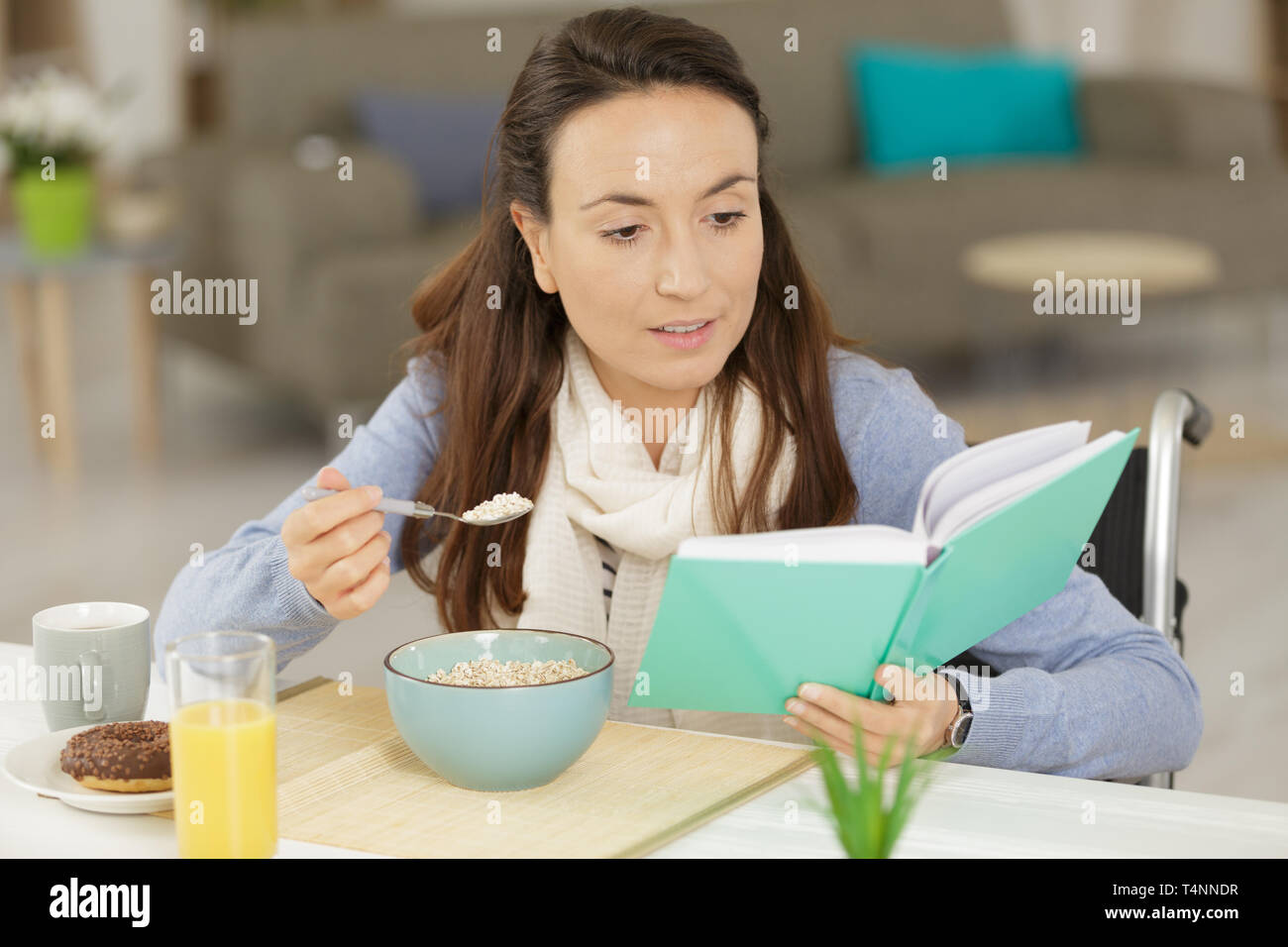 young disabled woman reading a book while eating breakfast Stock Photo