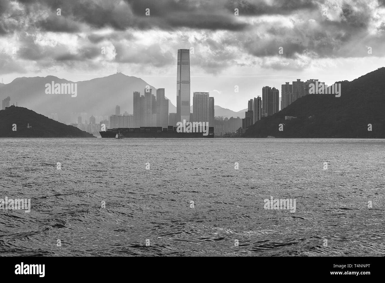 Moody Black And White Photo Of A Container Ship Passing In Front Of The Hong Kong Skyline As It Exits The East Lamma Channel Stock Photo